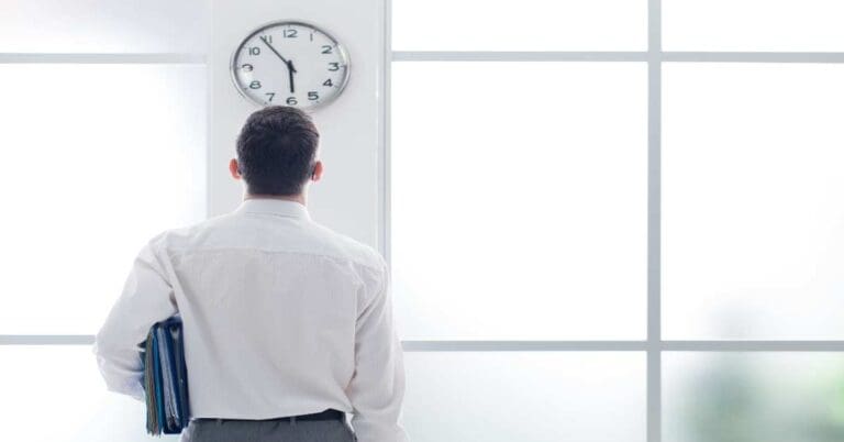 Businessman in the office staring at the clock, back view, time slave and stress concept